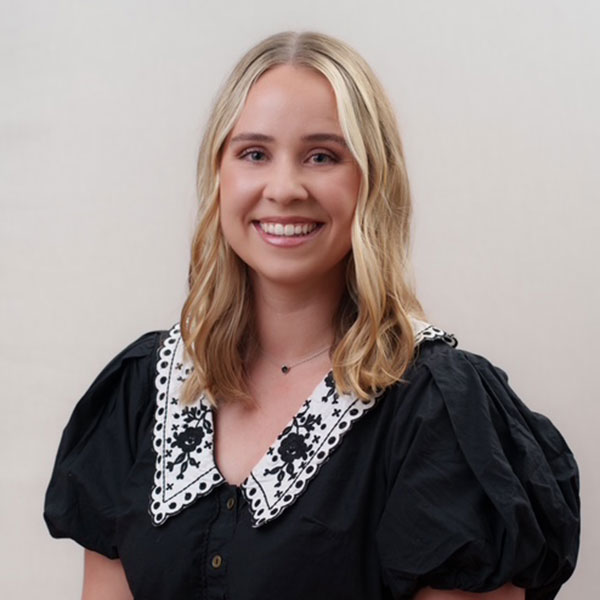 Smiling woman with shoulder-length blonde hair wearing a black blouse with a white embroidered collar.